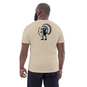 May include: Beige t-shirt with a black and white graphic on the back. The graphic depicts a cartoon figure wearing sunglasses, a Native American headdress, and holding a bow and arrow. The shirt is made of a soft material.