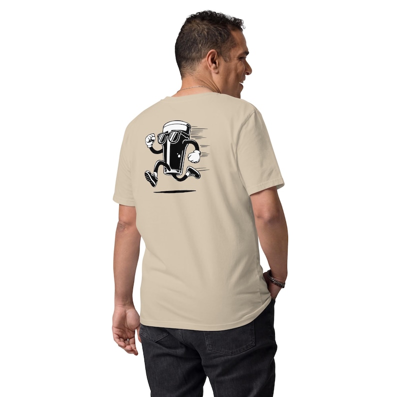 May include: Beige t-shirt with a black and white cartoon graphic of a running beer glass wearing sunglasses. The graphic has motion lines, suggesting speed. The shirt is made of a soft material.