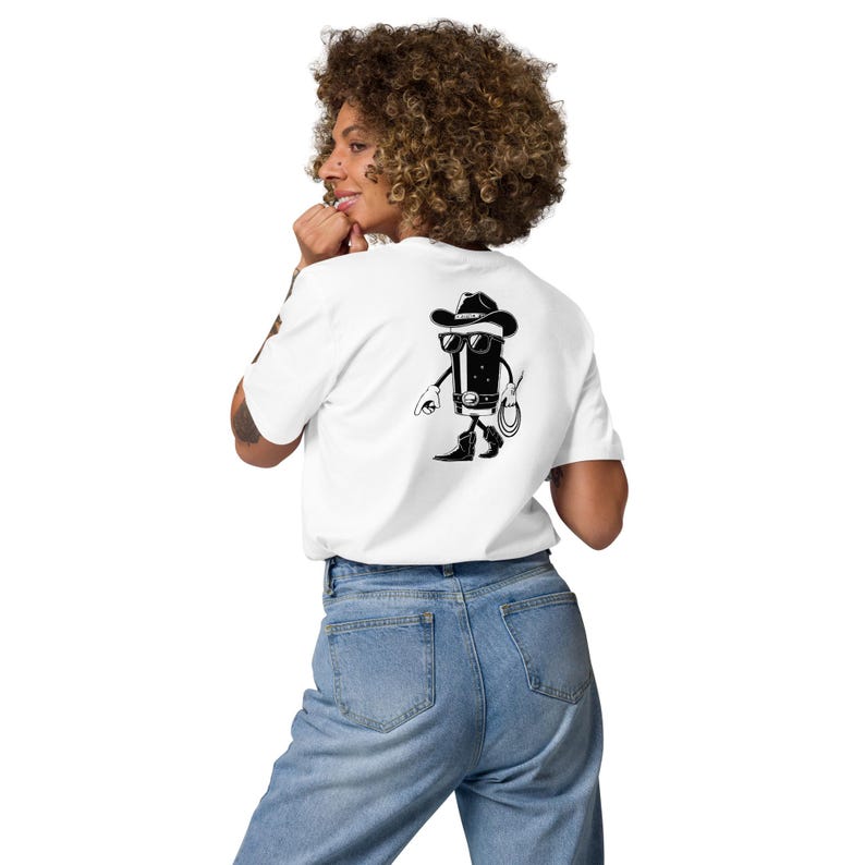 May include: White t-shirt with a black graphic of a cartoon cowboy character on the back. The cowboy is wearing a hat, sunglasses, and boots, holding a lasso. The shirt is made of a soft material.