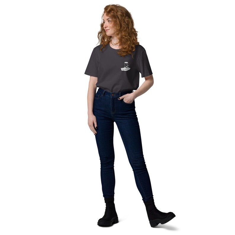 May include: A woman wearing a dark gray t-shirt with a small white graphic on the chest and dark blue jeans. The t-shirt has short sleeves and a crew neck. The jeans are high-waisted and fitted. She is wearing black ankle boots.