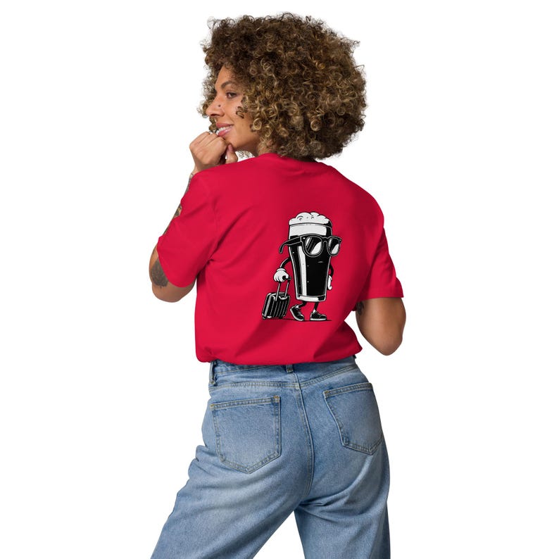 Puede incluir: Camiseta roja con un dibujo de una pinta de cerveza en blanco y negro con gafas de sol y una maleta. La persona lleva vaqueros azules.