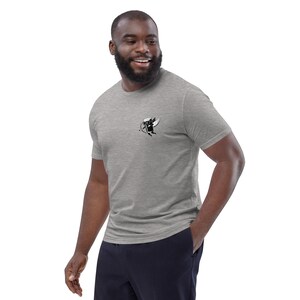 May include: A heather gray t-shirt with a small black and white graphic on the chest. The graphic appears to be a stylized image of a winged object with a bow and arrow. The shirt is short-sleeved and made of a soft material.