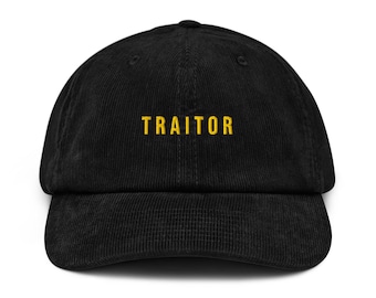 May include: A black corduroy baseball cap featuring the word TRAITOR embroidered in yellow capital letters across the front center panel. The hat has a structured crown, a curved brim, and a button at the top center of the cap.