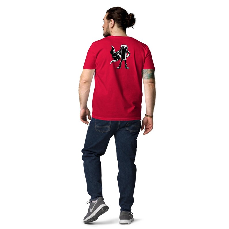 May include: A red t-shirt with a black and white graphic of a character with a cape. The person in the image is wearing blue jeans and grey trainers. The person is facing away from the camera.