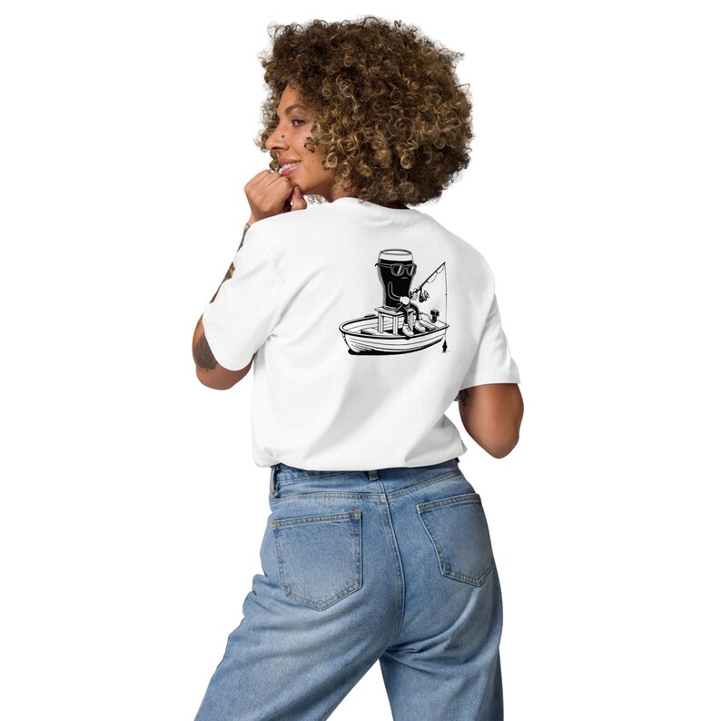 May include: White t-shirt with a black and white graphic of a boat with a person fishing. The person is wearing sunglasses and sitting in a boat with a motor. The t-shirt is made of a soft material.