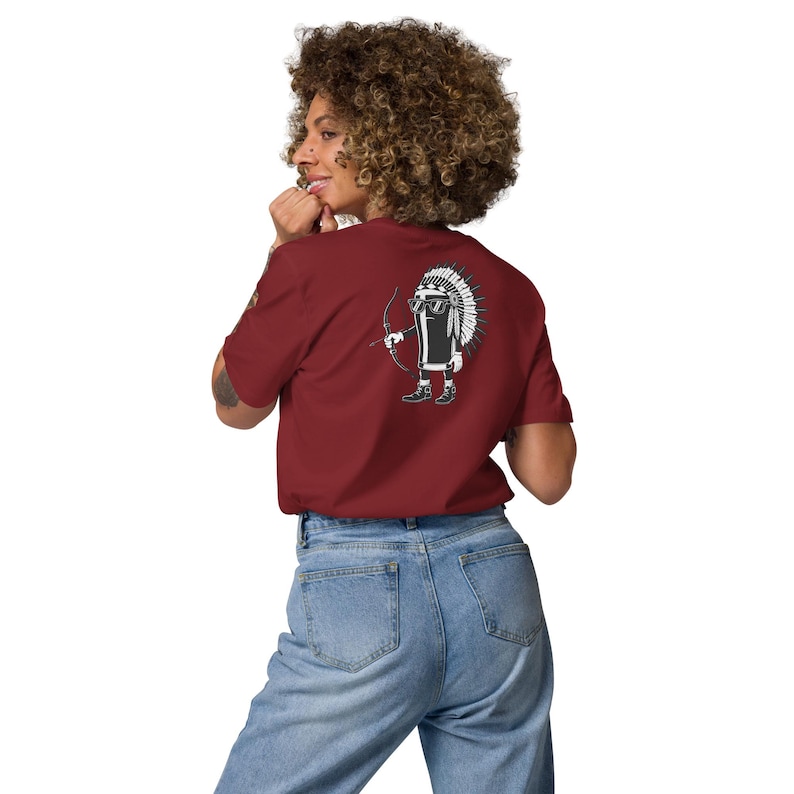 May include: A maroon t-shirt featuring a cartoon character with a Native American headdress, sunglasses, and a bow and arrow. The character is printed on the back of the shirt. The person in the image is wearing blue jeans.