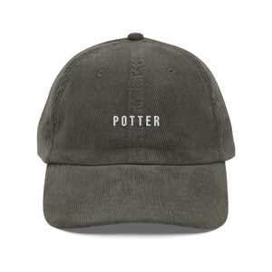 Puede incluir: Una gorra de béisbol de pana verde oscuro con la palabra "POTTER" bordada en blanco en la parte delantera.