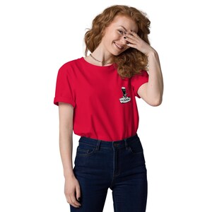 May include: A red t-shirt with a small graphic on the chest. The graphic is a black and white illustration of a coffee machine. The shirt is made of a soft material and has short sleeves.