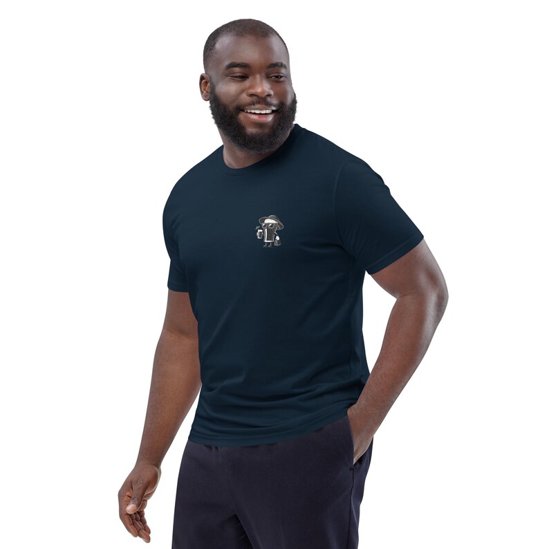 Puede incluir: Camiseta azul marino de manga corta con un peque&ntilde;o dise&ntilde;o bordado en el pecho. El dise&ntilde;o es una ilustraci&oacute;n estilizada de una persona con sombrero. La camiseta est&aacute; hecha de un material suave y c&oacute;modo.