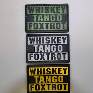 Può includere: Tre toppe rettangolari con la scritta "WHISKEY TANGO FOXTROT". La toppa superiore ha testo verde su sfondo nero, quella centrale testo bianco su nero e quella inferiore testo giallo su nero.