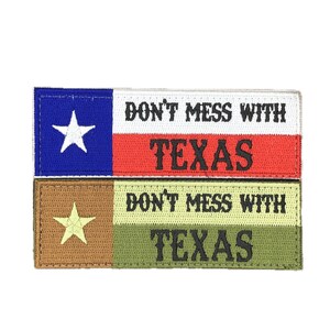 Peut inclure: Deux écussons brodés avec le texte "DON'T MESS WITH TEXAS". L'un des écussons présente les couleurs du drapeau du Texas : bleu, blanc et rouge. L'autre écusson a des couleurs marron, vert et jaune. Les deux écussons ont une étoile.