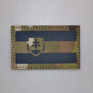May include: Rectangular patch featuring the Slovakian flag design. The patch has a dark blue horizontal stripe between two camouflage stripes. The Slovakian coat of arms is in the center.