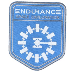 Puede incluir: Un parche bordado azul con las palabras "ENDURANCE SPACE EXPLORATION" en blanco. El parche presenta un diseño circular blanco con un centro central y formas rectangulares radiantes, todo dentro de un borde en forma de escudo.