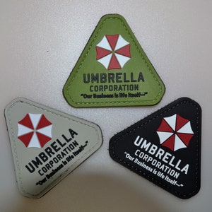 May include: Three triangular patches featuring the Umbrella Corporation logo. The patches are in green, beige, and black, each with a white and red umbrella logo and the text "UMBRELLA CORPORATION" and "Our Business is life itself..."