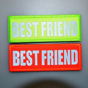 以下が含まれることがあります： 「BEST FRIEND」の文字が入った長方形のパッチが2つ。1つは蛍光グリーンで緑色の縁取り、もう1つは鮮やかな赤色で赤い縁取り。文字は銀色の太字です。