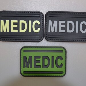 May include: Three rectangular patches with the word "MEDIC" in bold letters. One patch has a black background with yellow lettering, another has a black background with gray lettering, and the third has a green background with black lettering.