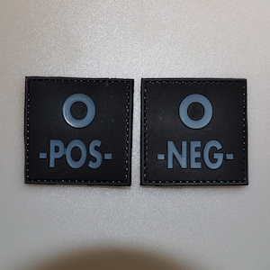 May include: Two black square patches with gray text and a gray circle. One patch reads "-POS-" and the other reads "-NEG-". The patches are likely for tactical gear or medical use.