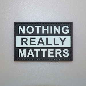 以下が含まれることがあります： 「NOTHING REALLY MATTERS」と書かれた白い文字が特徴の長方形の黒いパッチ。テキストは3行に配置され、「REALLY」の文字は水色の背景にあります。パッチにはステッチされた縁があります。