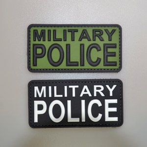 May include: Two rectangular patches with the words "MILITARY POLICE". The top patch has a green background with black lettering. The bottom patch has a black background with white lettering. Both patches have a black border.
