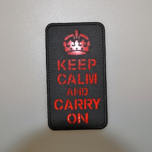 May include: Black rectangular patch featuring the phrase "KEEP CALM AND CARRY ON" in red, topped with a red crown. The patch has a textured surface.