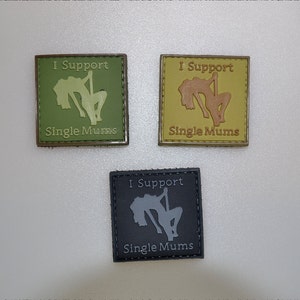 Puede incluir: Tres parches cuadrados con el texto "I Support Single Mums". Cada parche presenta una silueta de una persona bailando en barra. Los parches son de color verde oliva, beige y negro.