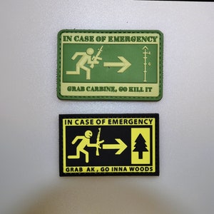 Può includere: Due toppe rettangolari con la scritta "IN CASE OF EMERGENCY". Una è verde con una figura che corre e la scritta "GRAB CARBINE, GO KILL IT". L'altra è nera con una figura che corre e la scritta "GRAB AK, GO INNA WOODS".