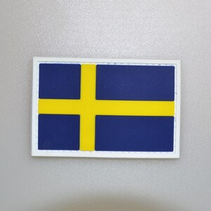May include: A rectangular patch featuring the flag of Sweden. The flag has a blue background with a yellow Nordic cross. The patch is framed by a white border.