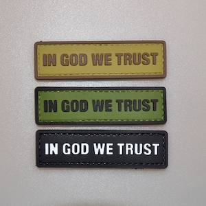 May include: Three rectangular patches with the text "IN GOD WE TRUST". The top patch is tan with brown text, the middle is olive green with black text, and the bottom is black with white text.