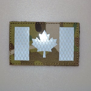 May include: A rectangular patch featuring the Canadian flag design. The flag includes a white maple leaf in the center and two white vertical bars on either side, set against a camouflage background.