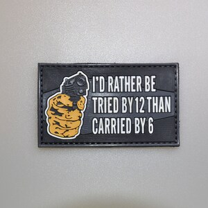 Peut inclure: Écusson rectangulaire noir avec le texte "I'D RATHER BE TRIED BY 12 THAN CARRIED BY 6". L'écusson présente un dessin d'une main tenant une arme à feu. La main et l'arme sont dans des tons de jaune, orange et noir.