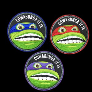 May include: Three embroidered patches featuring Teenage Mutant Ninja Turtles. Each patch has a different colored mask: blue, red, and purple. The text "COWABUNGA IT IS" is arched around the turtle's face. The turtles have green faces and white teeth.