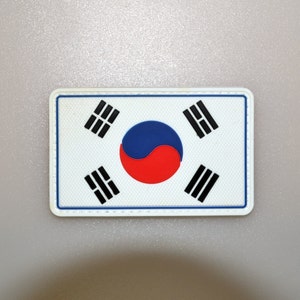 May include: Rectangular patch featuring the South Korean flag. The flag has a white background with a central yin-yang symbol in red and blue, and four black trigrams in each corner. The patch has a white border.