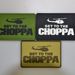 Może przedstawiać: Trzy prostokątne naszywki w kolorze oliwkowym, czarnym i beżowym. Każda naszywka przedstawia sylwetkę helikoptera nad napisem "GET TO THE CHOPPA" pogrubioną czcionką. Naszywki są prawdopodobnie przeznaczone do sprzętu wojskowego lub taktycznego.