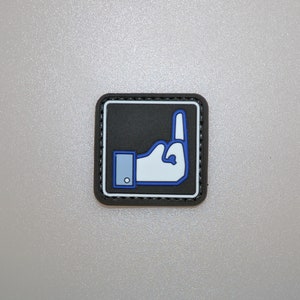 May include: Square patch featuring a white hand giving the middle finger, outlined in blue, set against a black background. The patch has a blue cuff and a black border with white stitching.