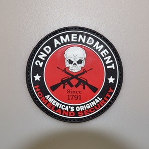 May include: A round patch with a black border and the text "2ND AMENDMENT" in white. The center features a red circle with a white skull, crossed rifles, and the text "Since 1791". The bottom text reads "AMERICA'S ORIGINAL HOMELAND SECURITY".