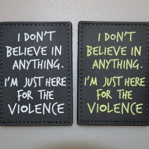 Pode incluir: Dois patches retangulares pretos com texto branco e amarelo. O texto nos patches diz: "EU NÃO ACREDITO EM NADA. EU SÓ ESTOU AQUI PELA VIOLÊNCIA."
