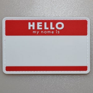 Puede incluir: Una etiqueta rectangular con una sección superior roja que dice "HELLO my name is" en letras blancas. El cuerpo principal de la etiqueta es blanco, con un borde rojo en la parte inferior. La etiqueta está diseñada para la personalización.