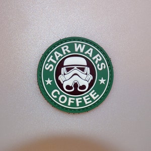 May include: A round, green and white patch with the text "STAR WARS COFFEE" encircling a white Stormtrooper helmet design. The patch is a parody of the Starbucks logo, with a brown background.