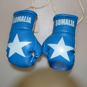 May include: Two small blue boxing gloves with white stars and the word "SOMALIA" printed in white. The gloves are connected by a beige string.