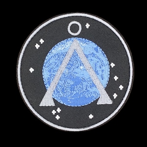 Può includere: Una toppa circolare con sfondo nero, raffigurante un pianeta azzurro con un triangolo bianco e un cerchio bianco in alto. Forme bianche a forma di stella sono sparse attorno al cerchio.