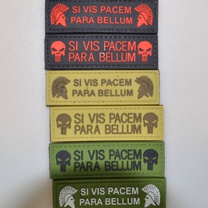 May include: A collection of rectangular patches in various colours, including black, red, and green. Each patch displays the Latin phrase "Si Vis Pacem Para Bellum." Some feature a Spartan helmet, others a skull, suitable for tactical use.