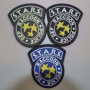May include: Three embroidered patches with the text "S.T.A.R.S. Raccoon Dep Police" and three yellow stars. The patches are black, white, and blue with yellow and white text.