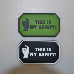Op de afbeelding: Twee rechthoekige patches met de tekst "THIS IS MY SAFETY!". Eén patch is groen met zwarte tekst en een handafbeelding. De andere is zwart met witte tekst en een witte handafbeelding.
