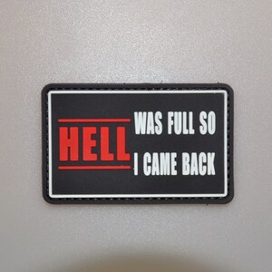 May include: Black rectangular patch with the words "HELL" in red and "WAS FULL SO I CAME BACK" in white. The patch has a black border and is set against a gray background.