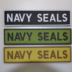 May include: Three rectangular patches with the text "NAVY SEALS". The top patch is black with white lettering, the middle is olive green with black lettering, and the bottom is tan with brown lettering. All patches have a stitched border.