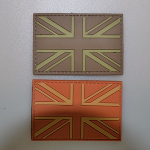 May include: Two rectangular patches featuring the Union Jack flag design. One patch is tan with a light green design, and the other is orange with a yellow design. Both patches have a stitched border.