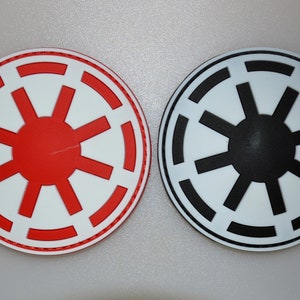 May include: Two round emblems with a white background and a red or black starburst design. The red emblem has a red border, while the black emblem has a black border. These are likely themed items.