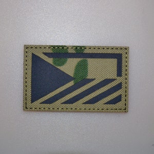 May include: Rectangular patch with a camouflage background and a dark blue geometric design. The design includes a triangle and diagonal stripes. The patch is bordered with black stitching.