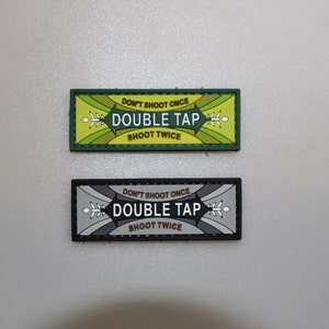 Könnte beinhalten: Zwei rechteckige Aufnäher mit dem Text "DON'T SHOOT ONCE DOUBLE TAP SHOOT TWICE". Einer ist grün mit gelben und weißen Akzenten, der andere ist schwarz und grau mit weißen Akzenten. Beide Aufnäher haben ein dekoratives Design.