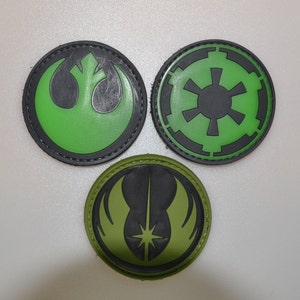 May include: Three circular patches with black edging. The top left patch displays a green symbol on a black base. The top right patch has a green symbol on a black base. The bottom patch features a green and black symbol.